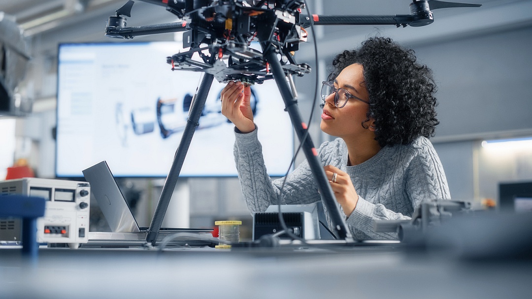 junge schwarze Frau mit Brille stell in einem Forschungslabor an einem technischen Gerät etwas ein.