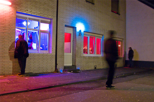 Straßenszene mit Bordell: Ein Mann schaut in ein hellerleuchtetes Fenster, ein zweiter läuft vorbei, ein dritter geht um die nächste Ecke