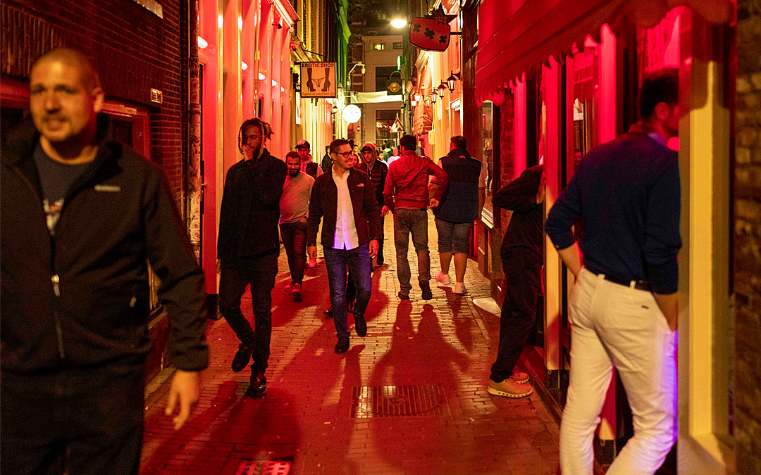 In einer rotbeleuchteten Gasse laufen mehrere Männer, die sich neugierig umschauen