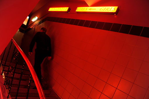 Ein Mann steigt eine Treppe zu einem Bordell hoch. Der Hausflur ist rotbeleuchtet.