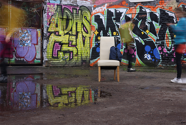 Vor einer Wand mit viel Graffiti steht ein weißer Stuhl, ein blauer Beutel liegt darauf.