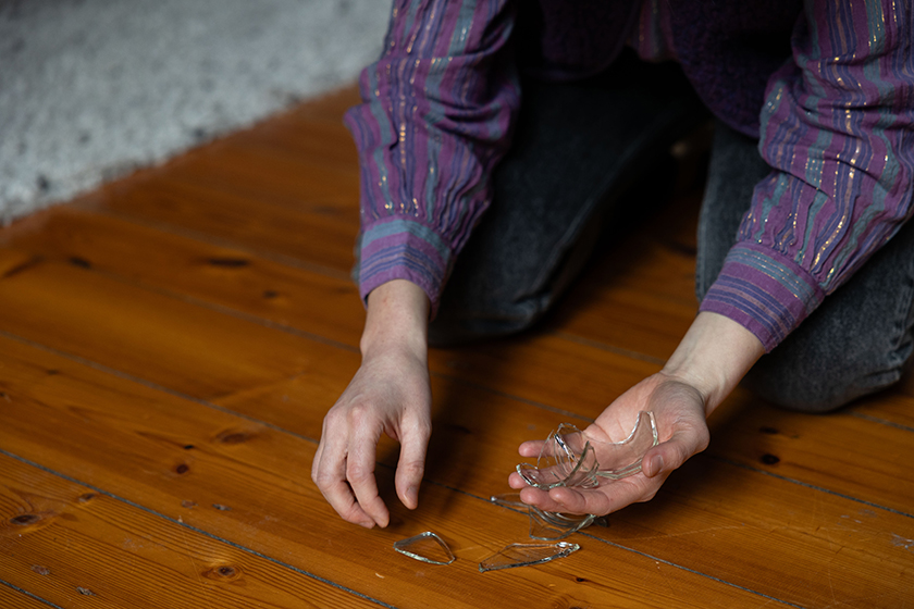 Frau sammelt Glasscherben vom Boden in ihrer Hand
