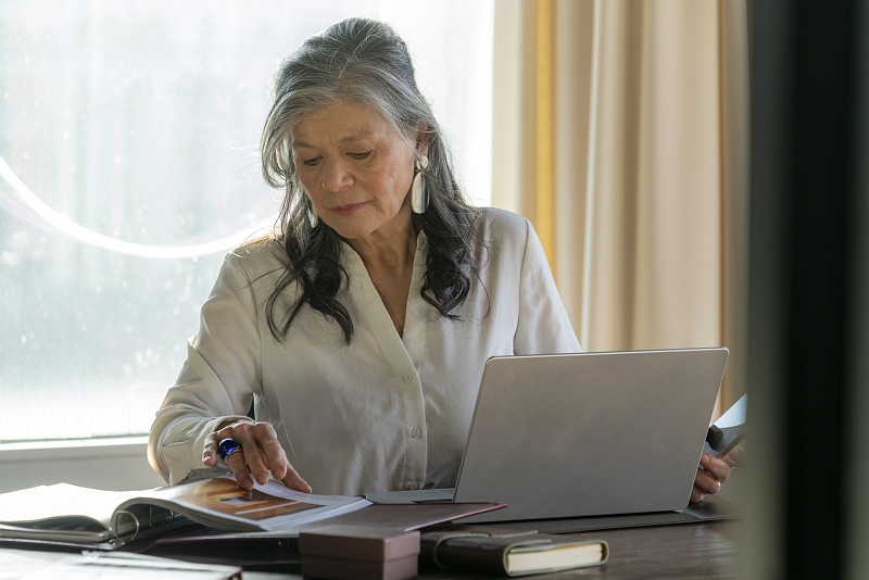Frau mit grauen Haaren arbeitet konzentriert am Schreibtisch