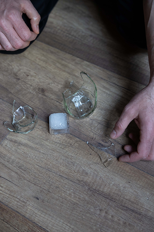 Männerhände heben Scherben eines zerbrochenen Glases vom Boden auf
