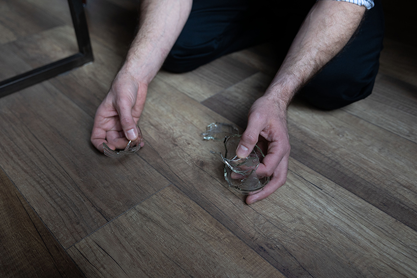 Männerhände heben Glasscherben vom Boden auf