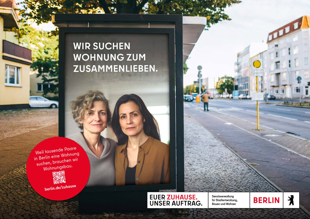 Plakat an einer Berliner Bushaltestelle zeigt ein nett lächelndes Lesbenpaar im mittleren Alter. Text: Wir suchen Wohnung zum Zusammenleben.