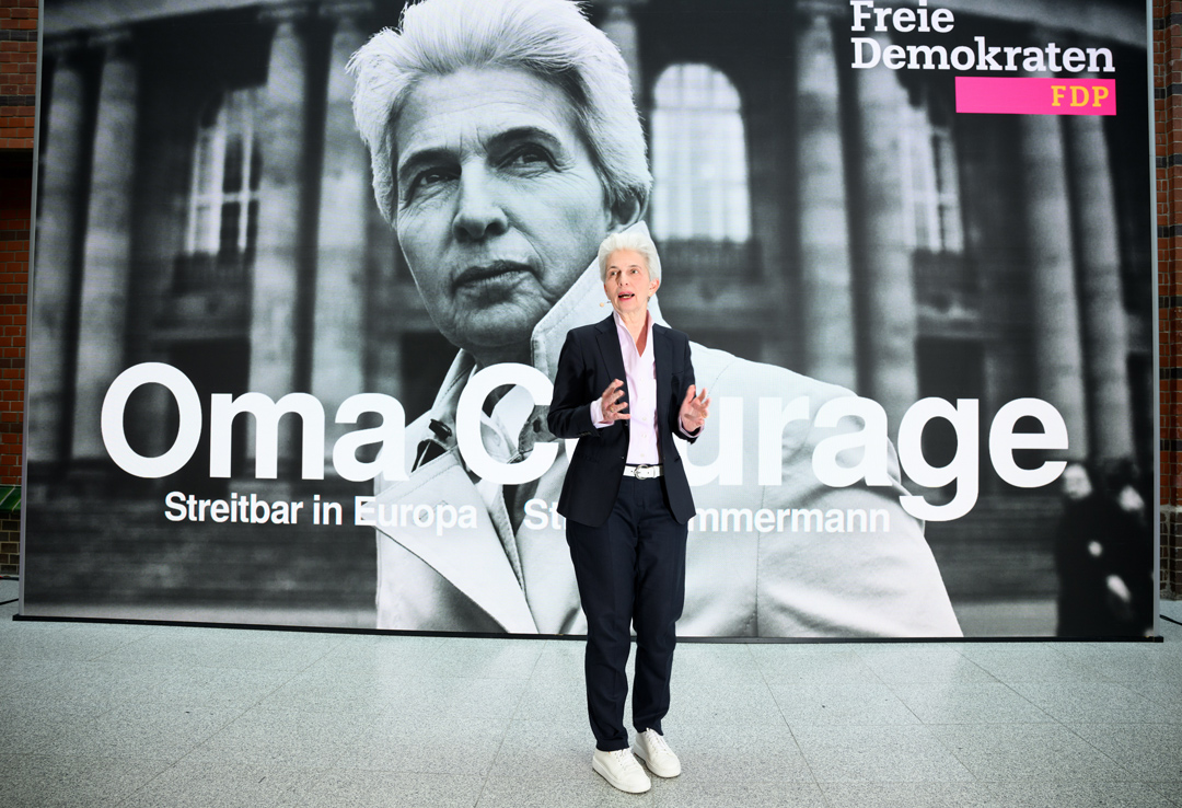 Marie-Agnes Strack-Zimmermann steht vor dem Wahlplakt mit Text "Oma Courage"