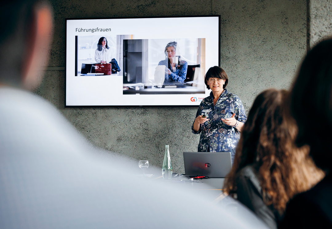 Frau steht bei ihrem Vortrag vor einer PowerPointPräsentation mit zwei Fotos aus dem Fotoprojekt Führungsfrauen