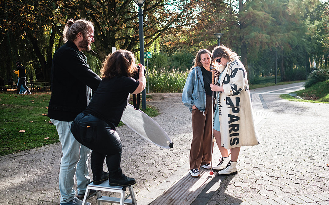 Kleinwüchsige Fotografin steht auf einer Trittleiter und fotografiert zwei Frauen