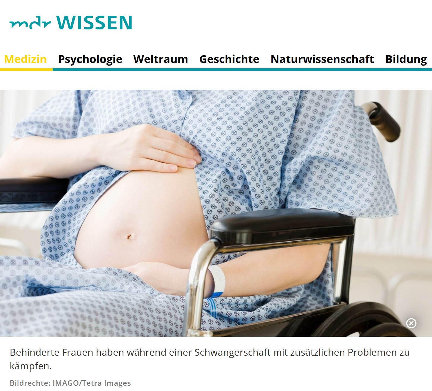 Auf einem Rollstuhl sitzt eine Schwangere, sie hat das Krankenhaus-Hemd hochgeschoben, so dass ihr nackter Babybauch zu sehen ist. Ihr Kopf ist nicht zu sehen.